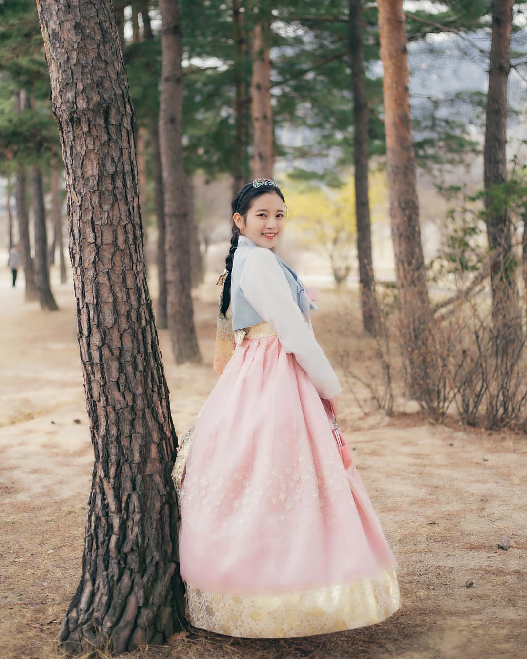 Visitor in a pink hanbok standing among trees