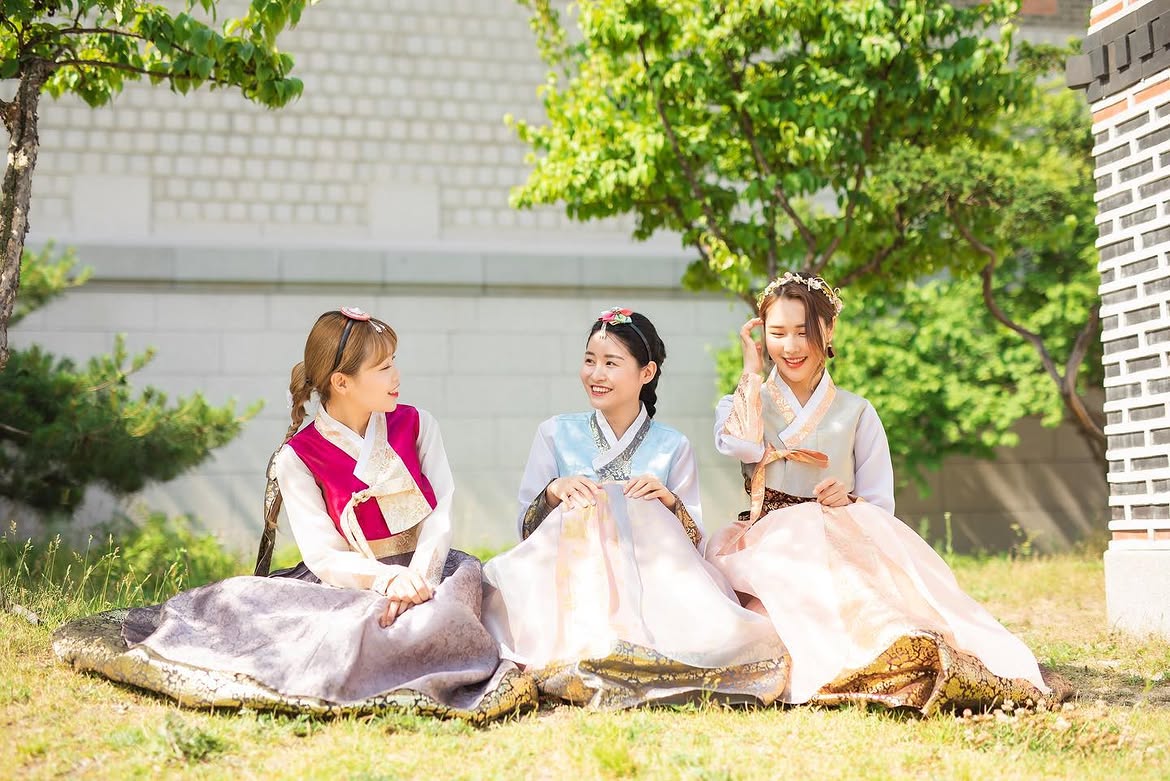 Three visitors in hanbok sitting on a lawn
